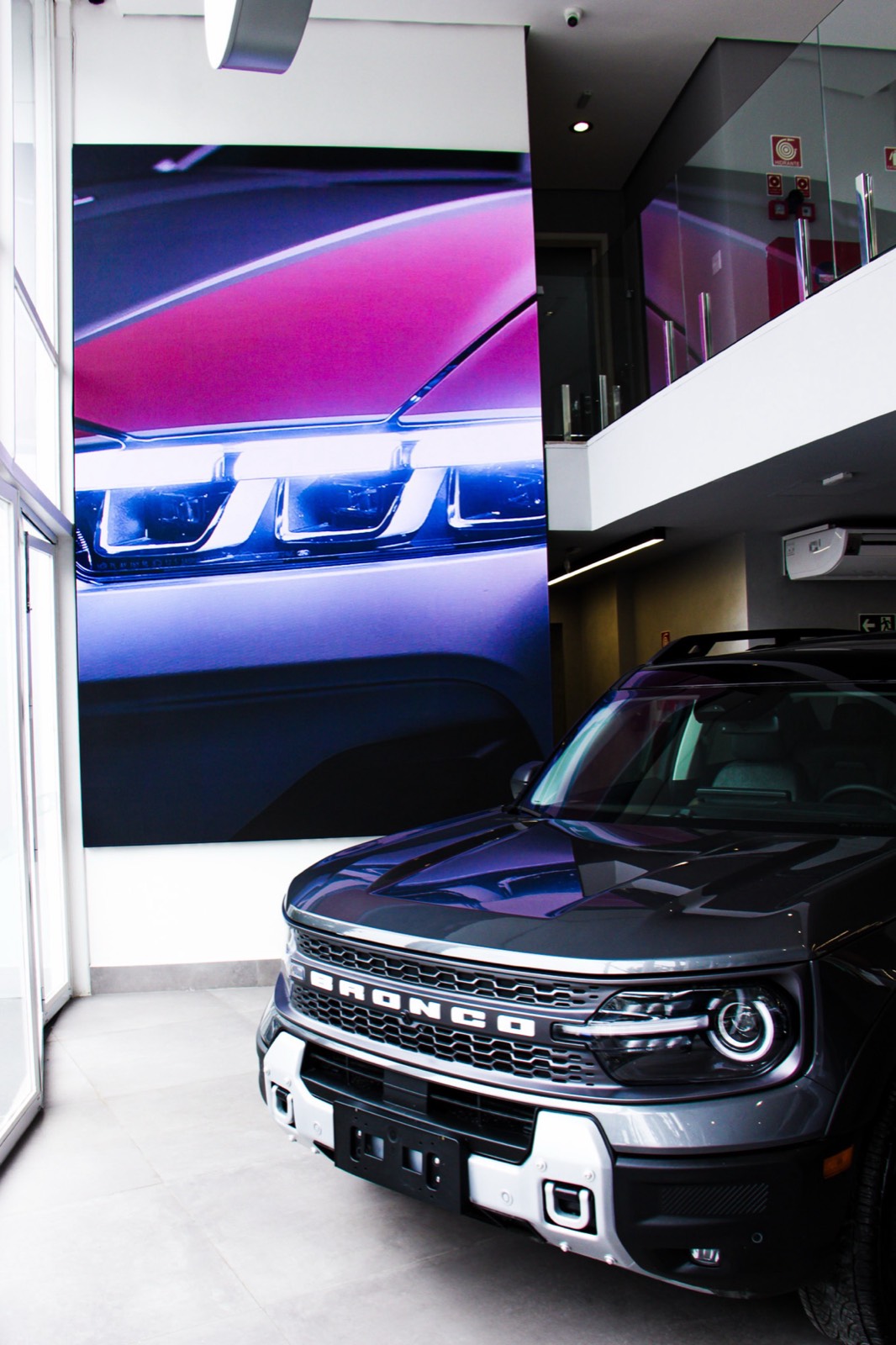 Painel de LED indoor vertical exibindo imagem de veículo, ao lado de um Ford Bronco Sport