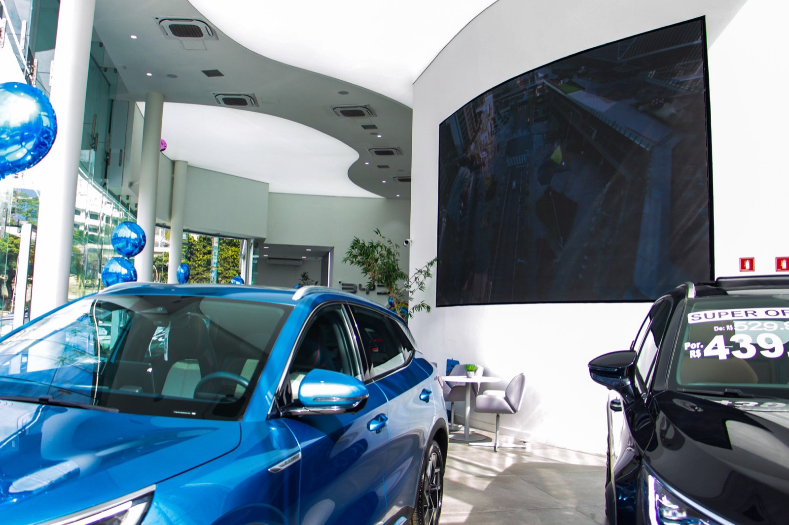 Painel de LED indoor apagado em uma parede curva do showroom, ao lado de carros expostos