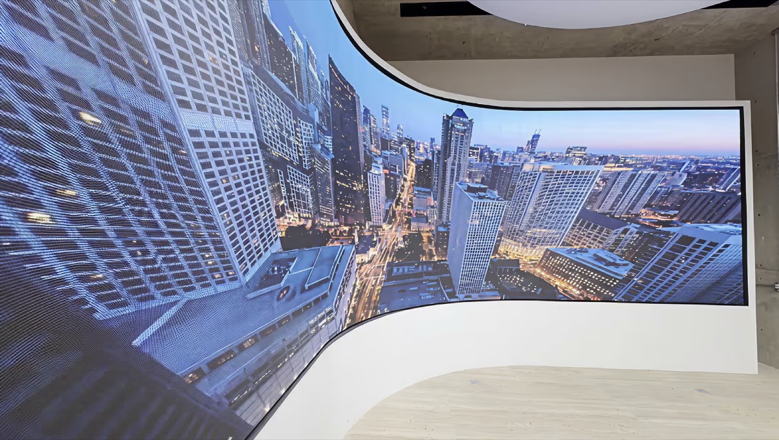 Painel de LED curvo indoor acompanhando a parede do showroom, com imagem aérea de prédios