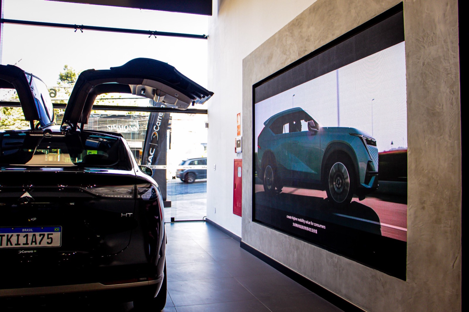 Painel de LED indoor emoldurado na parede do showroom GAC, ao lado de um carro com portas abertas