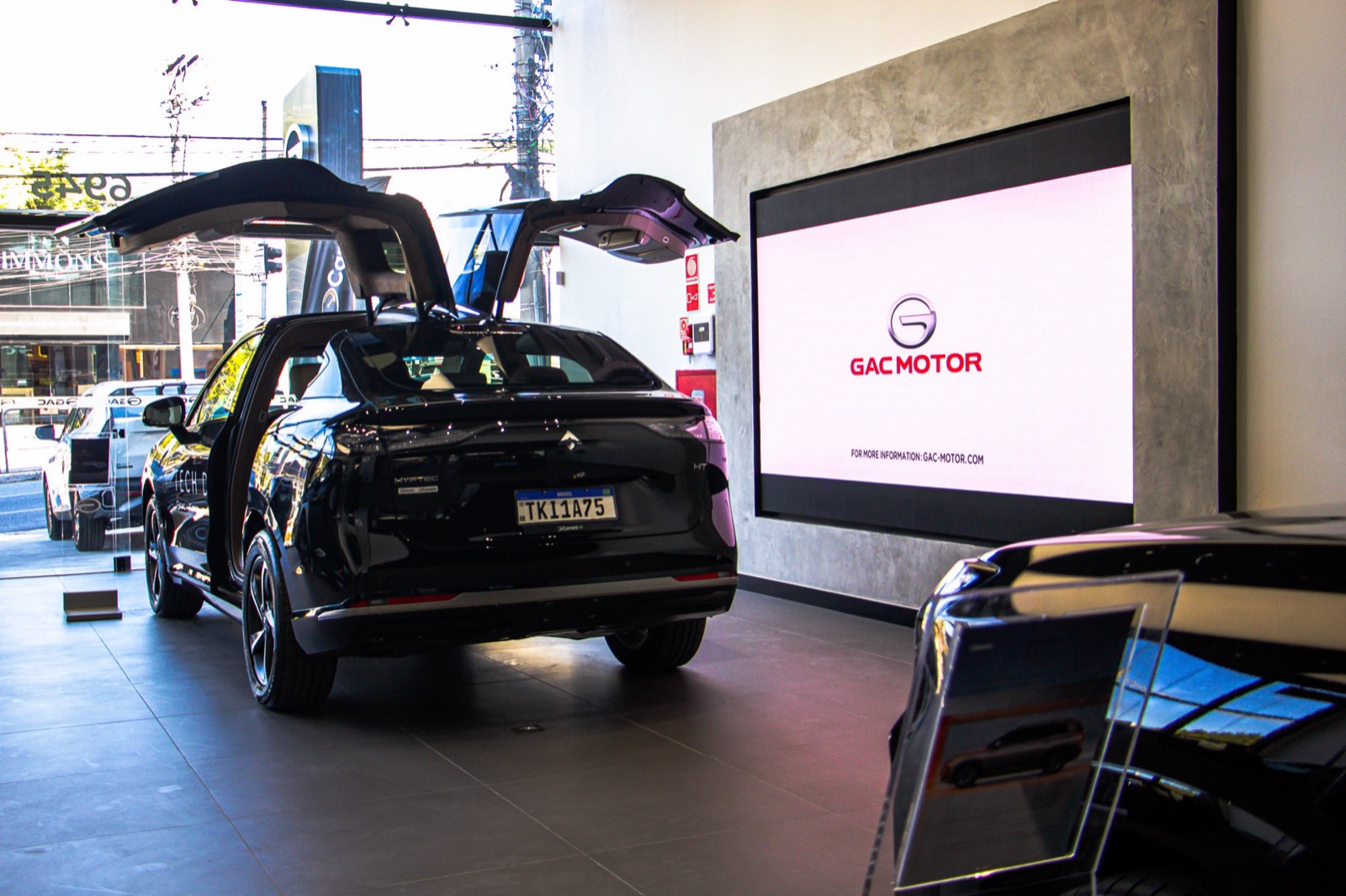 Painel de LED rosa com o logotipo GAC Motor, atrás de um carro com as portas em asa de gaivota abertas