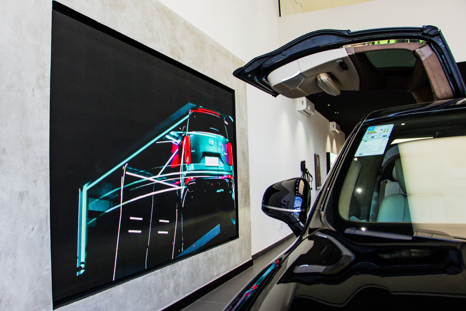 Painel de LED indoor exibindo um desenho técnico de carro, ao lado do porta-malas aberto de um GAC