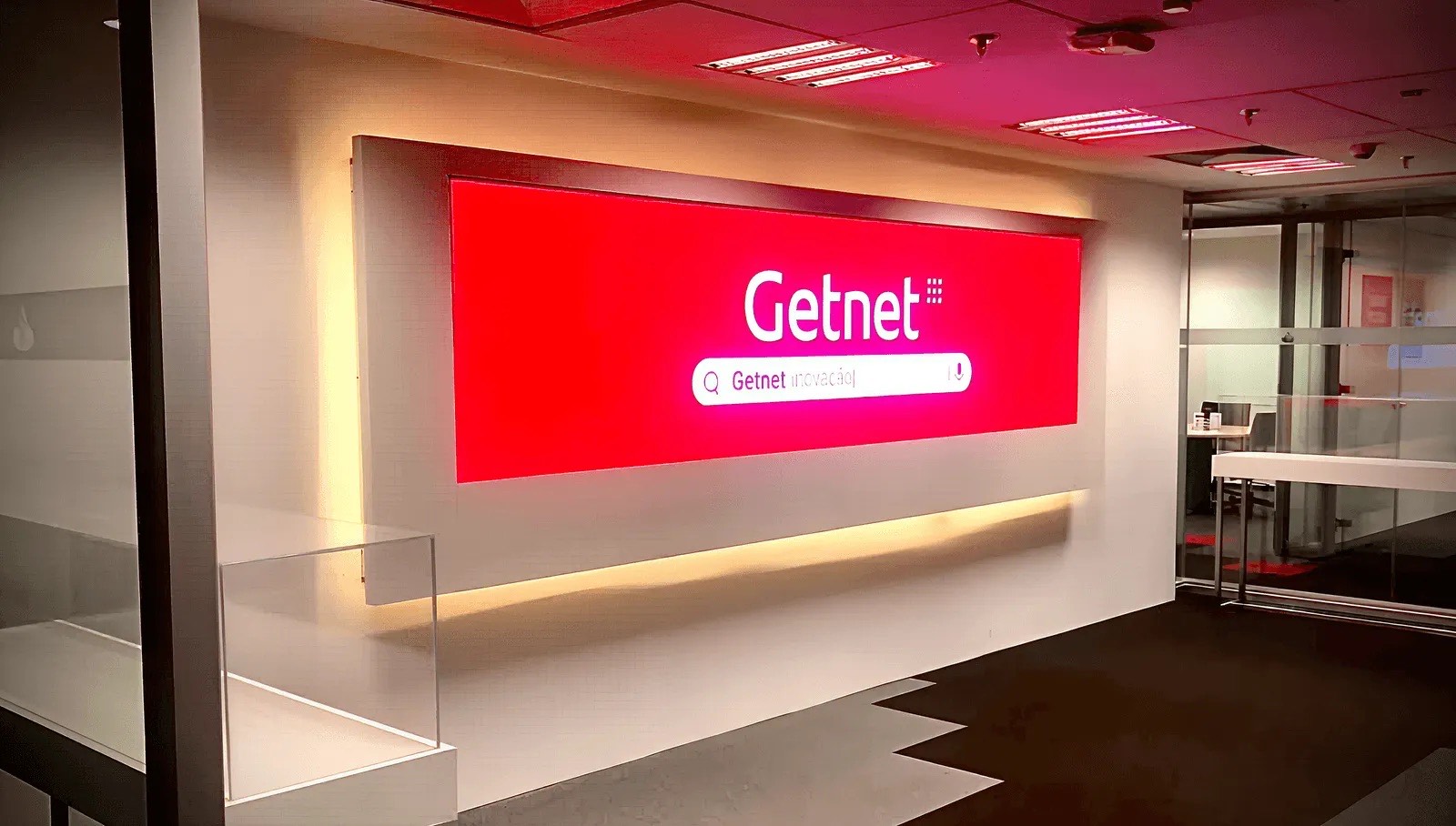 Painel de LED indoor vermelho com o logotipo Getnet em uma parede iluminada, na Vila Olímpia