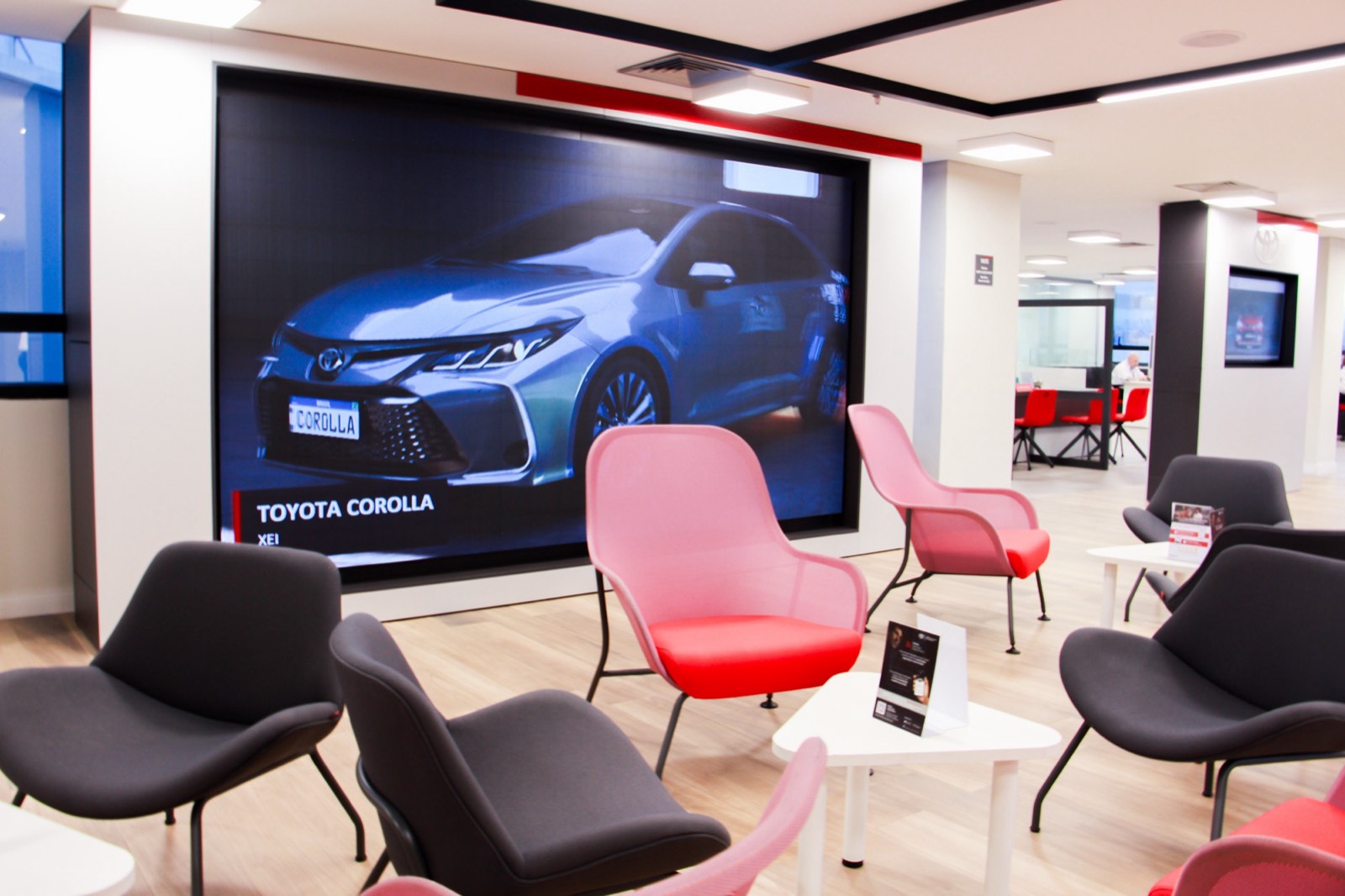 Painel de LED indoor com um Toyota Corolla na sala de espera da concessionária, com poltronas vermelhas