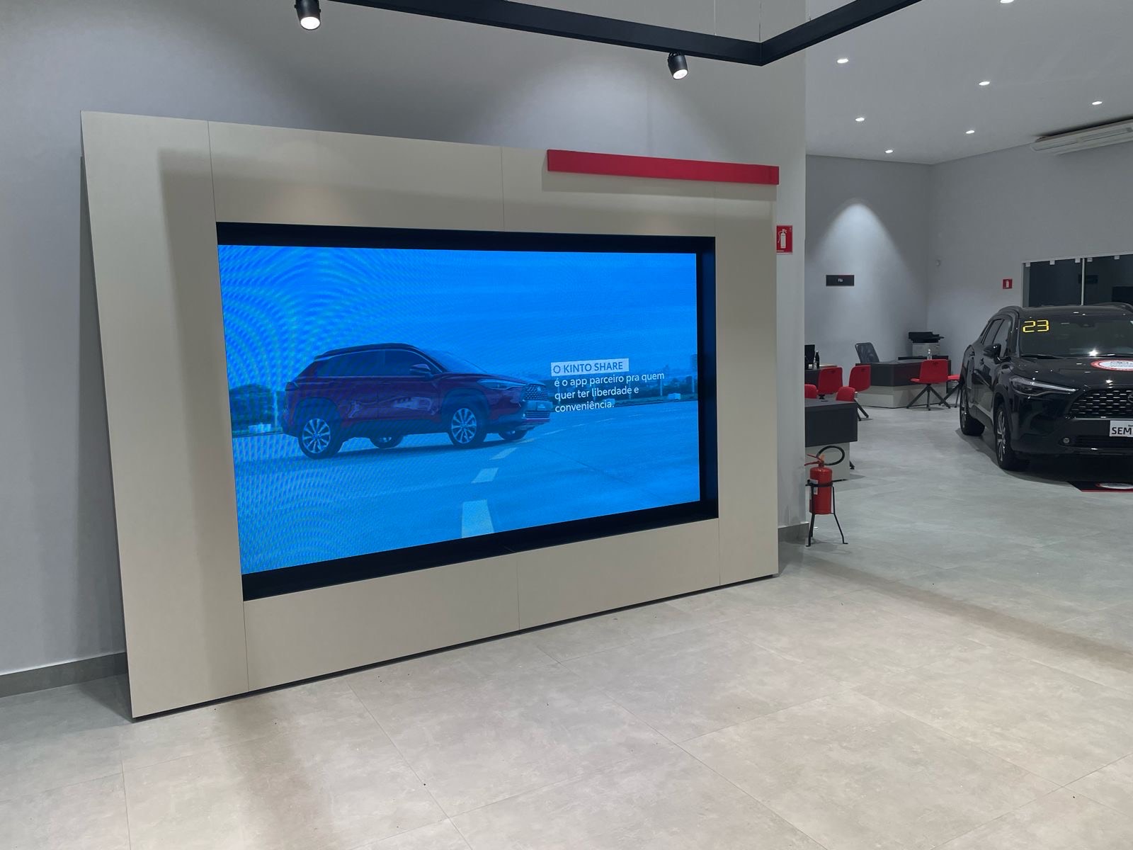 Monitor profissional de grande formato em moldura bege exibindo um carro, na concessionária Toyota