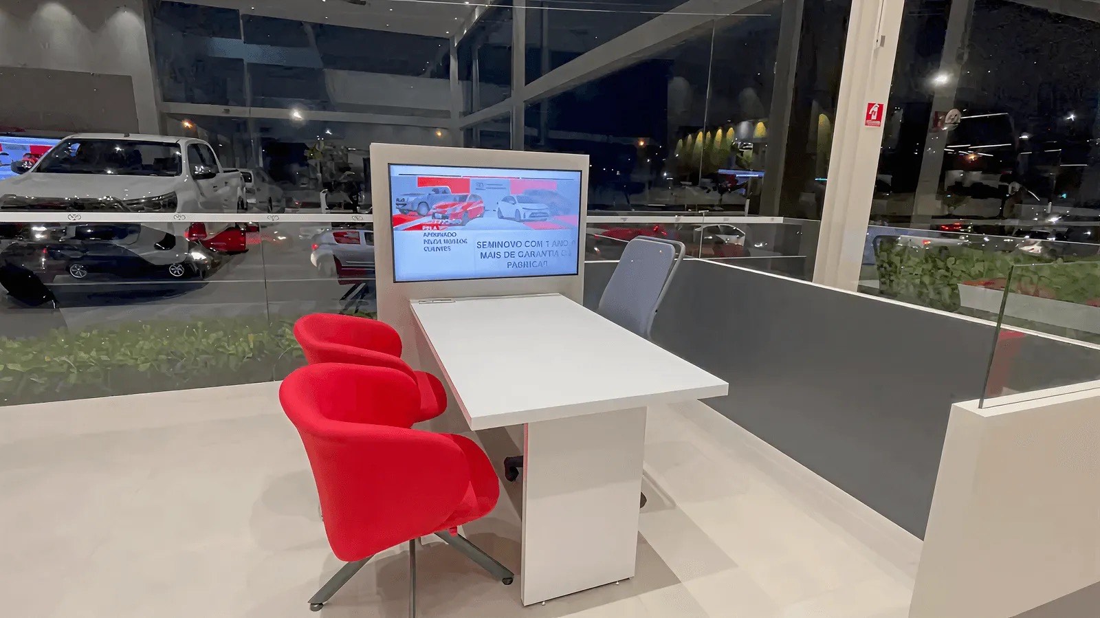 Monitor de grande formato com mesa de atendimento e cadeiras vermelhas na concessionária Toyota da Radial Leste