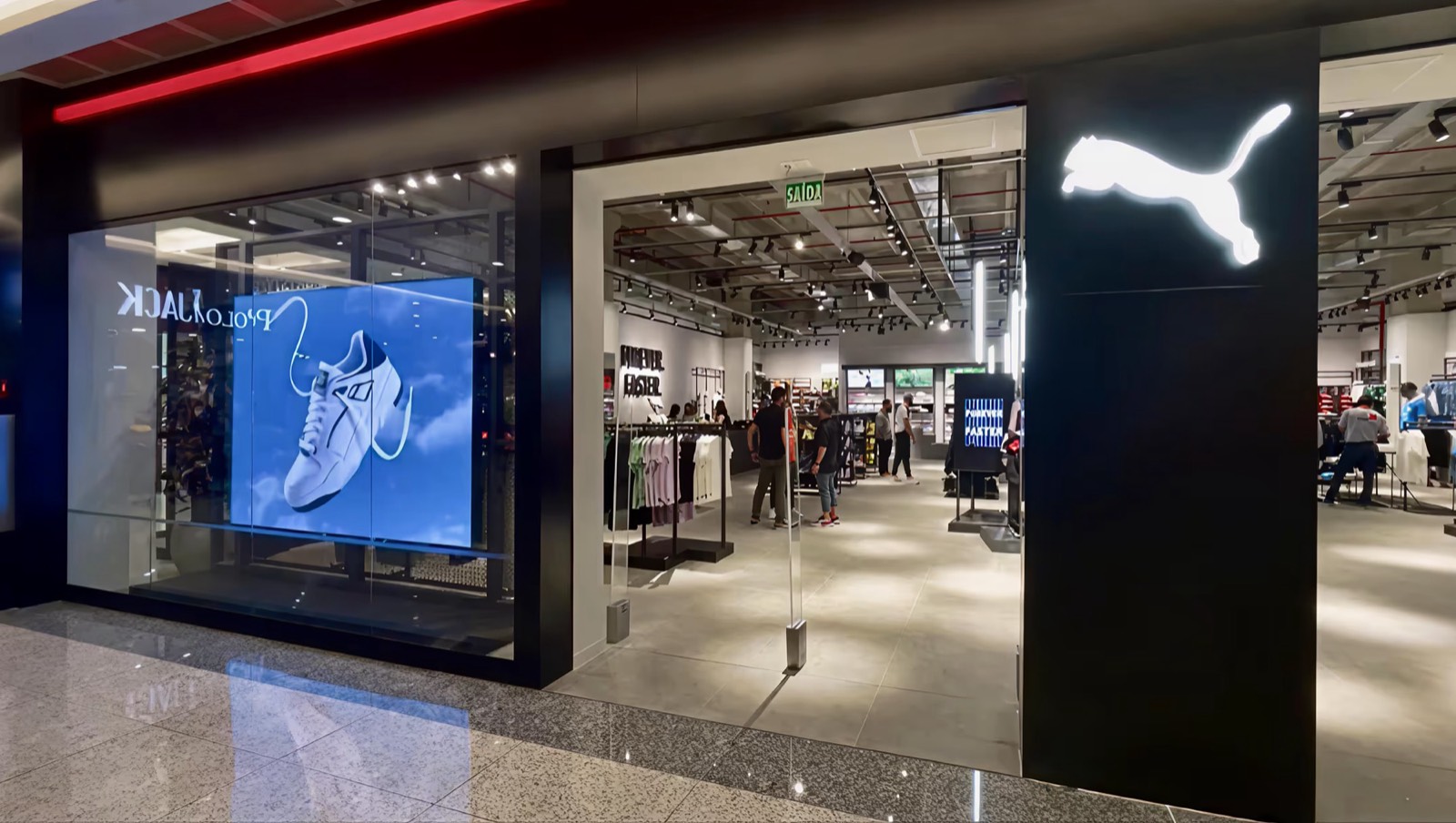 Vitrine da loja Puma com painel de LED exibindo um tênis, vista do corredor do shopping