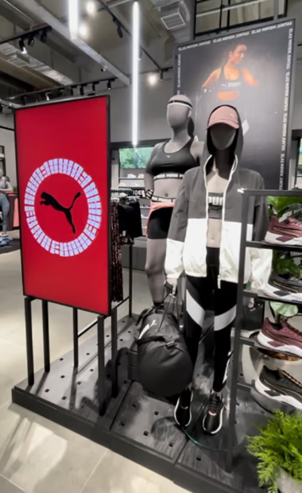 Totem vertical vermelho com o logotipo Puma e animação luminosa circular, ao lado de manequins