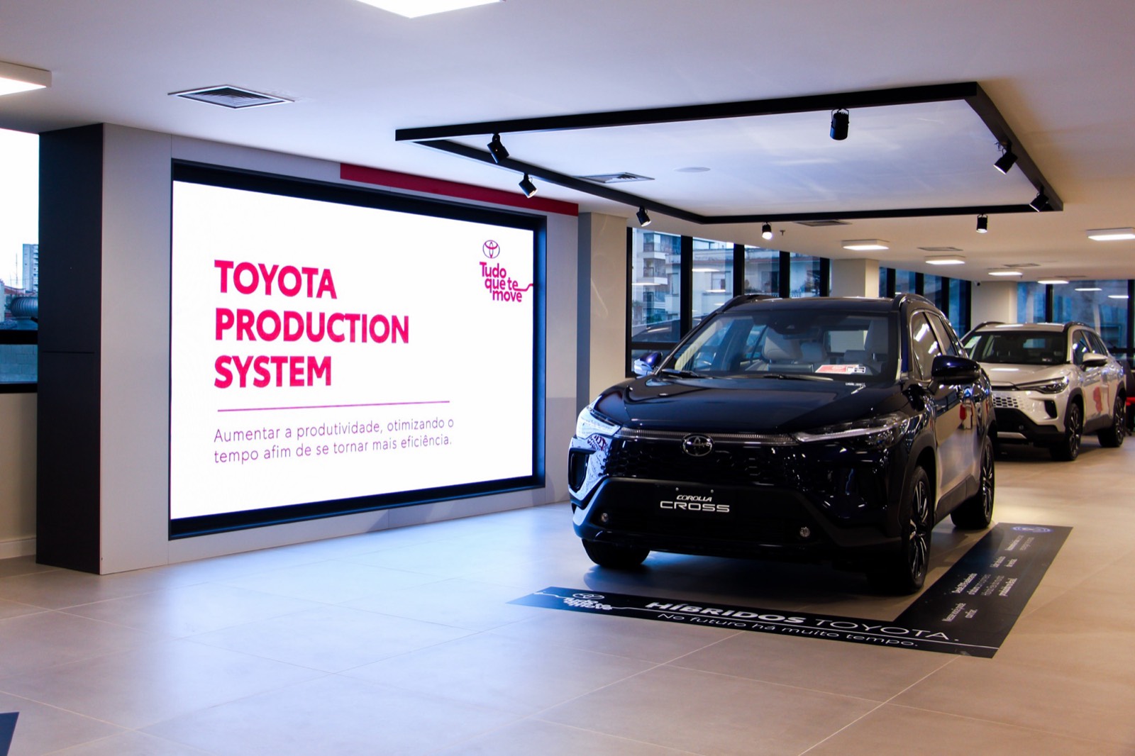 Painel de LED indoor com a mensagem Toyota Production System, ao lado de um carro no showroom