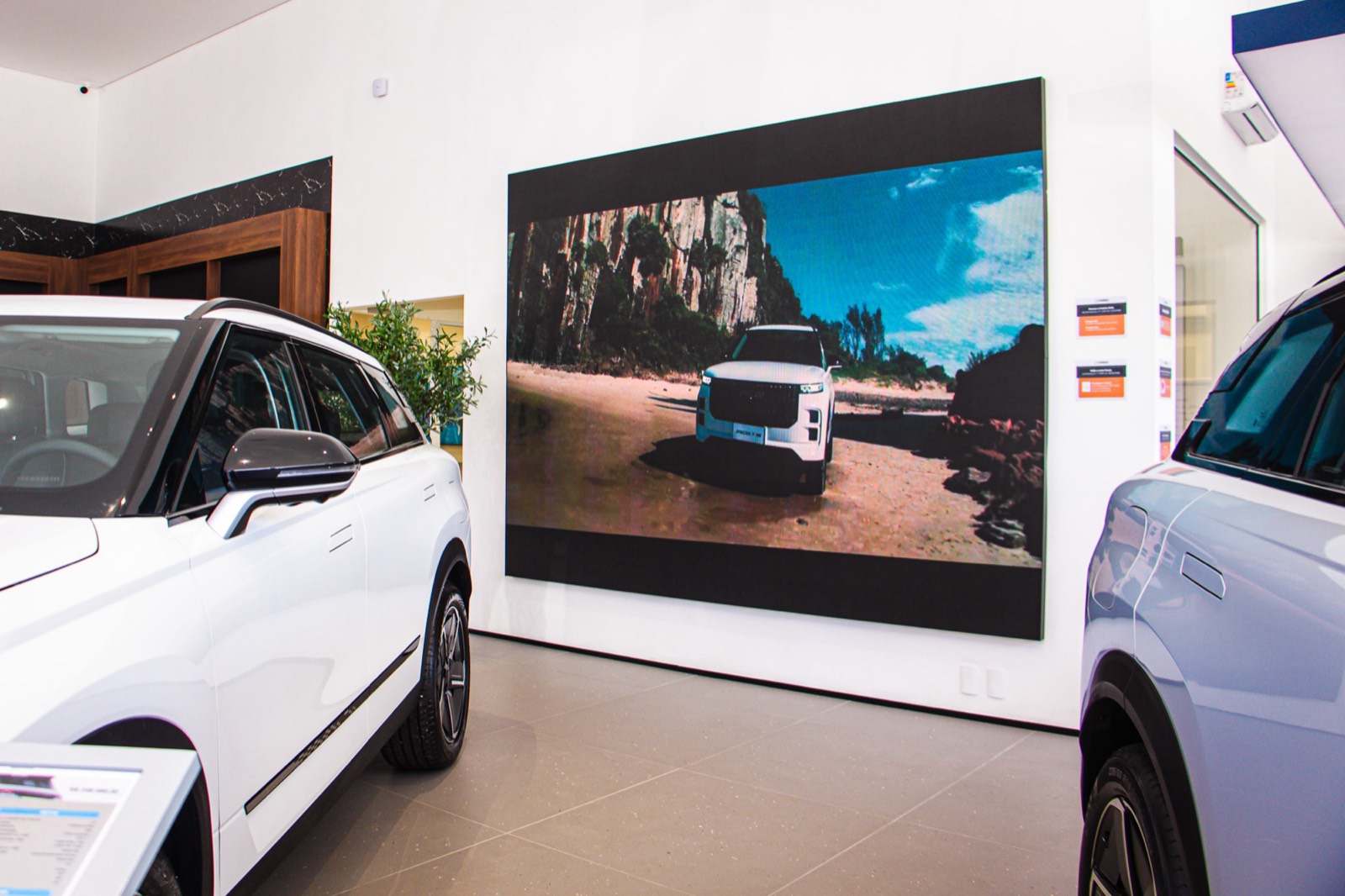 Painel de LED indoor exibindo um carro, com um veículo branco em primeiro plano na concessionária Omoda