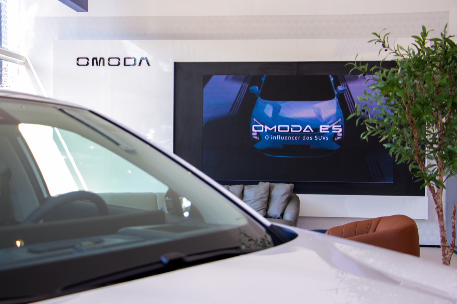 Painel de LED com o logotipo Omoda e a imagem de um carro azul, ao fundo do showroom