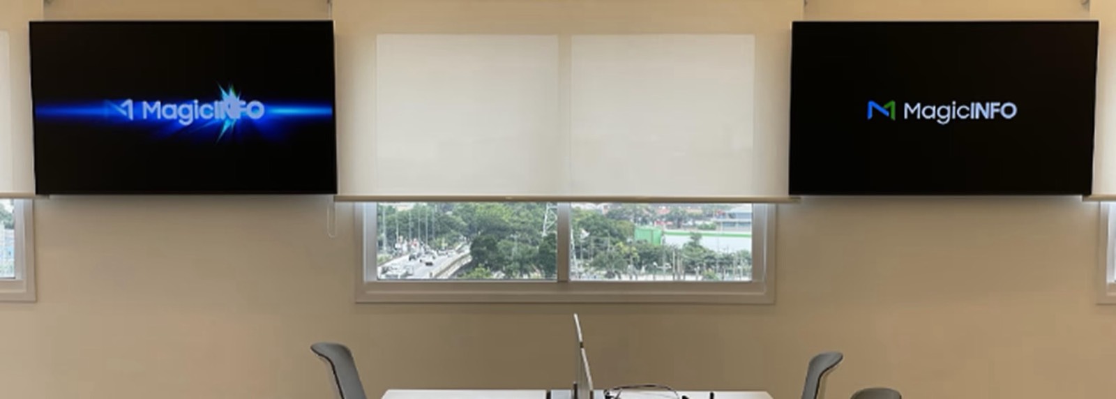 Dois monitores profissionais lado a lado em uma sala de reunião da Vila Leopoldina, ao lado de uma janela