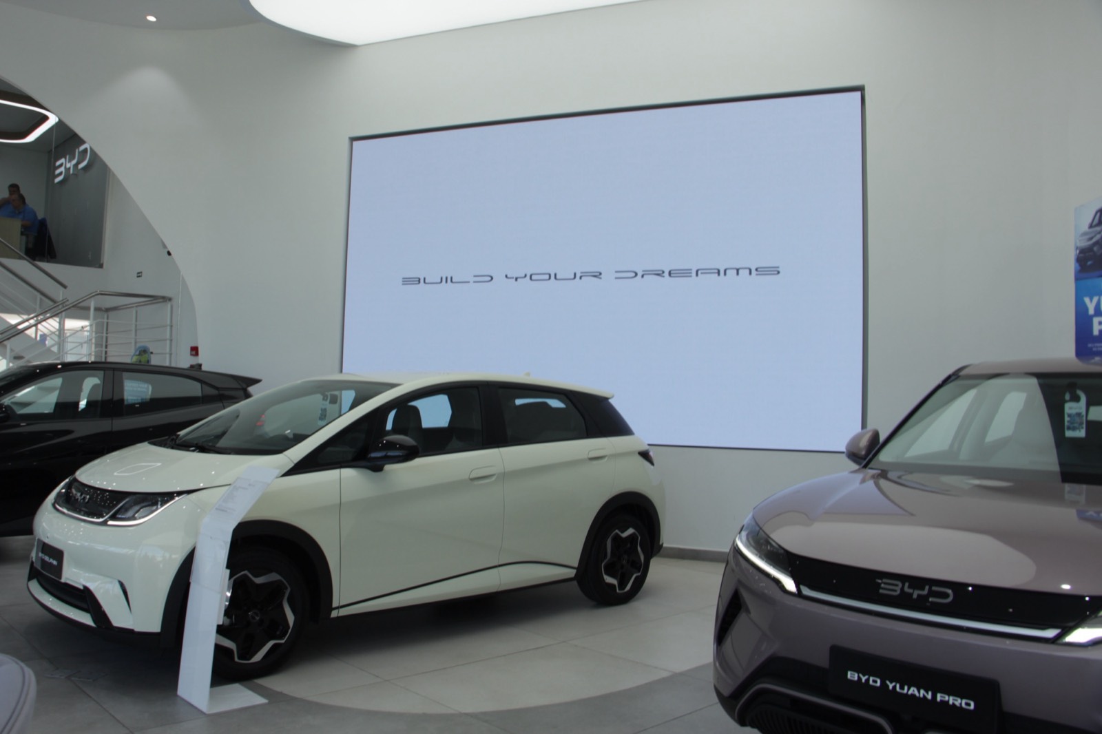 Painel de LED instalado na parede de uma concessionária, entre dois carros BYD